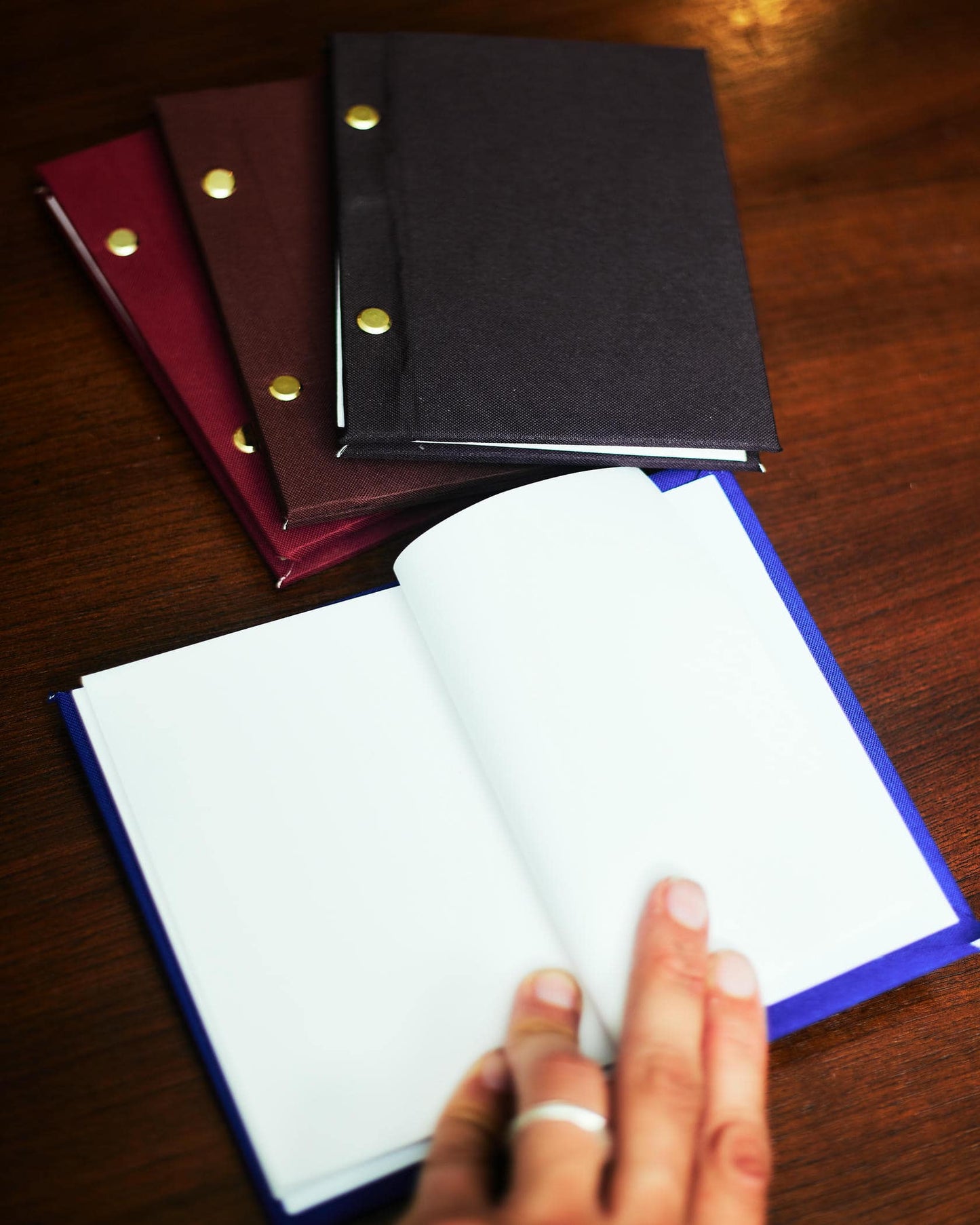 Three notebooks with different cover colors on a wooden surface, one open to show white pages.