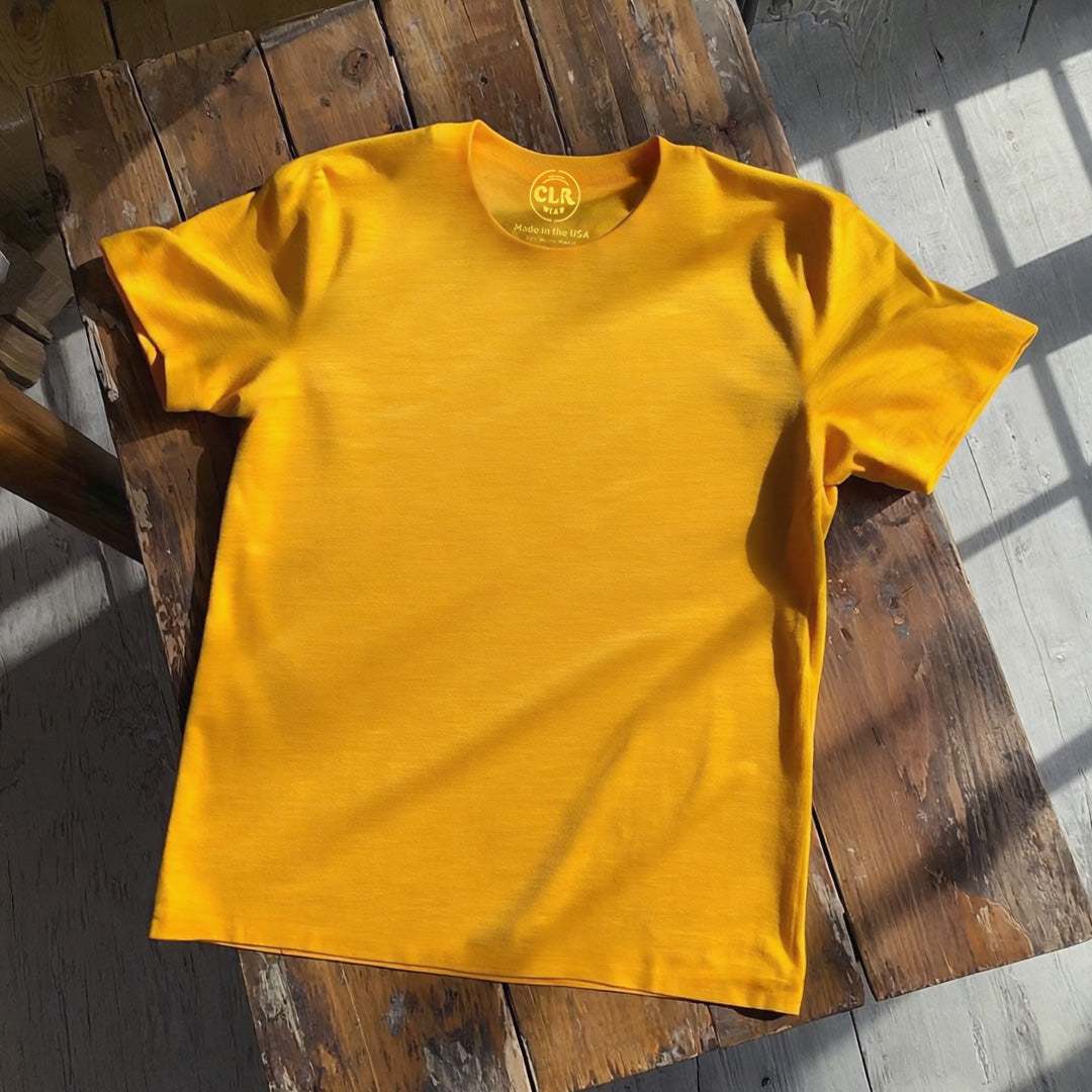 Yellow Basic Tee on rustic wooden table, raw-edged design, sunlight highlighting soft micro-modal fabric.